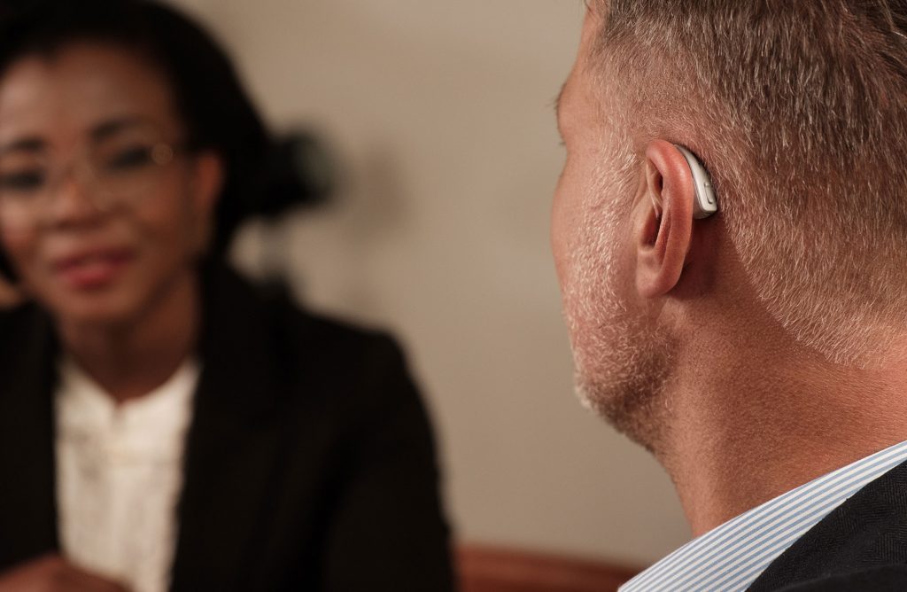 A photo of a man wearing bose lexi hearing aids with a woman looking on in the background