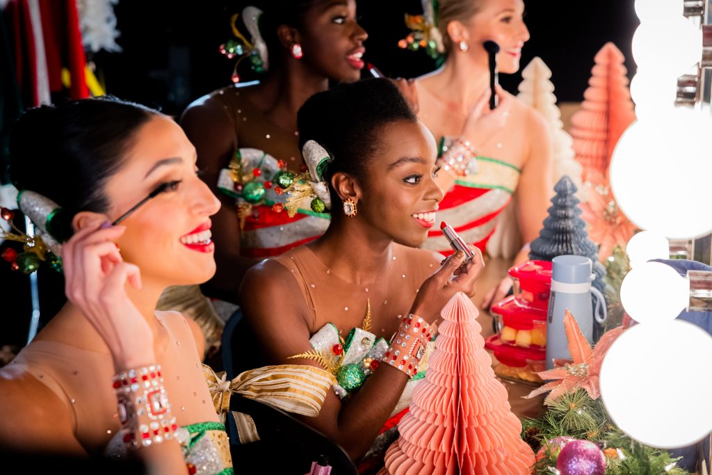 A Photo of the Radio City Rockettes applying QVC brand makeup in front of a lighted mirror