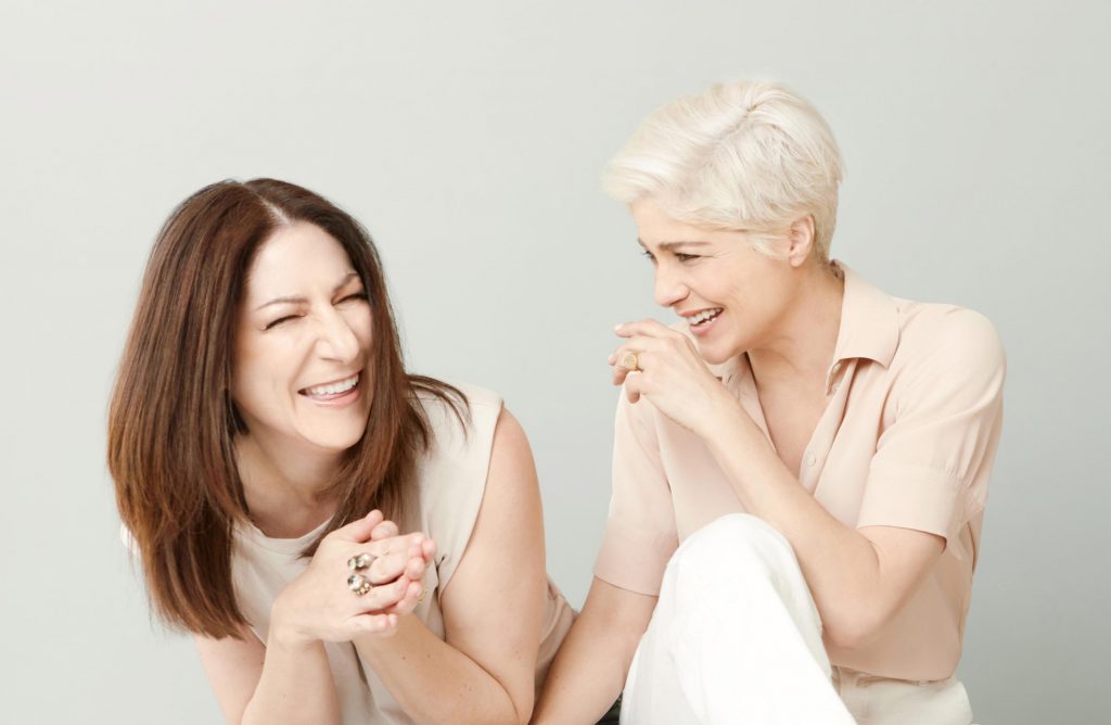 Two women in light clothing laughing together.